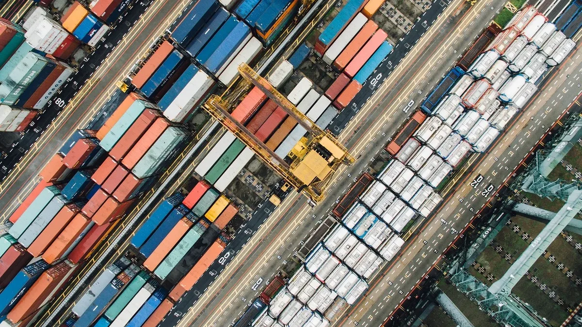 A large number of shipping containers, stacked horizontally and vertically, with some on train tracks and others on the ground, in a port or yard setting.